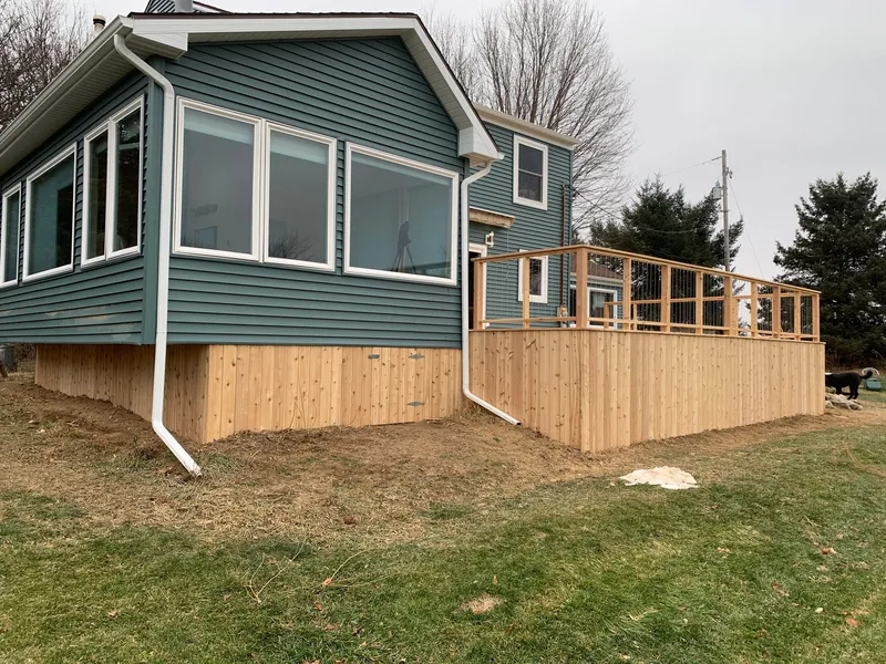 Raised deck with a new wood skirt beside a blue-sided sunroom.