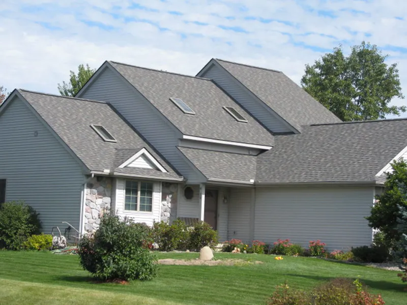 Gray home under a multi-gabled architectural shingle roof with skylights, against a blue sky.