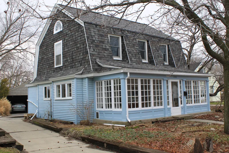 Blue house with a gray gambrel roof and a glazed front porch.