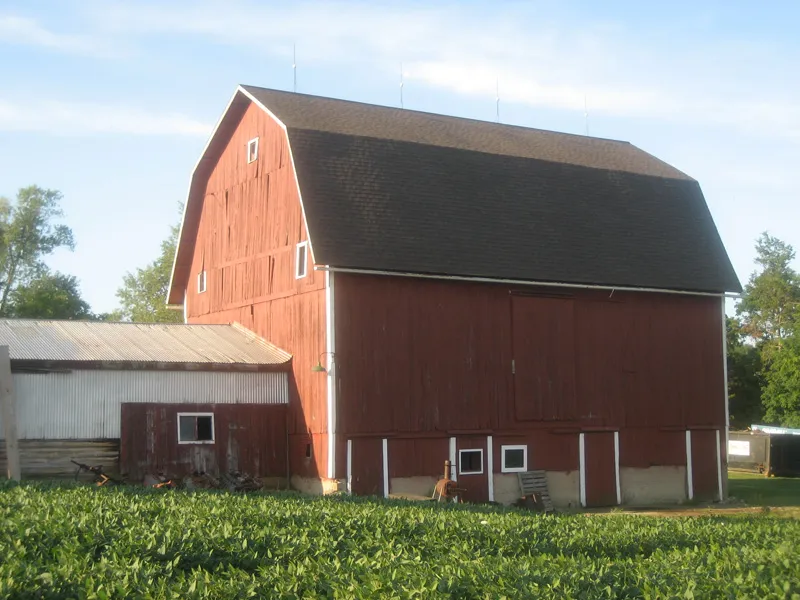 Red gambrel barn with a brown shingle roof.