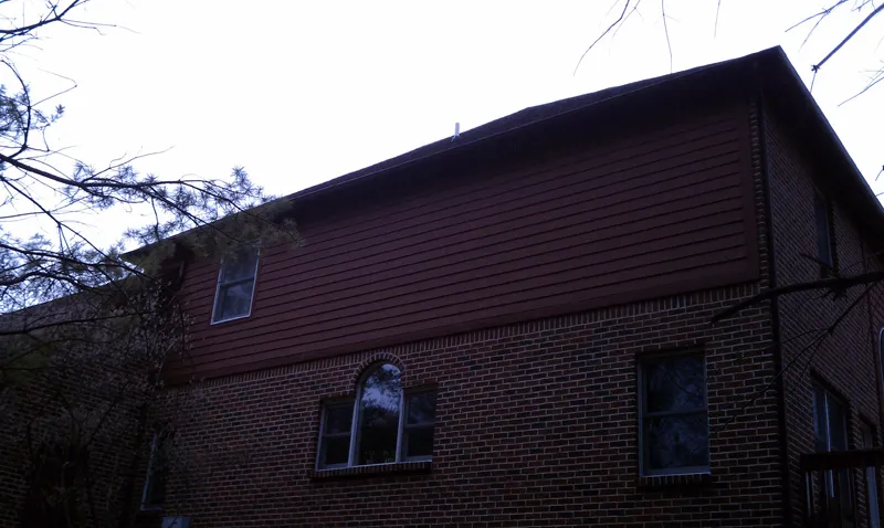 Before: upper story of a brick home with dark, weathered red siding.