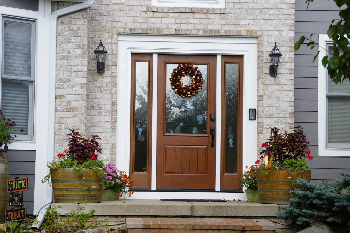 Wood-tone front door with sidelights in a brick entry, flanked by planters.