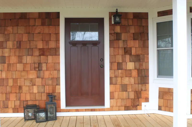 Craftsman-style front door set in natural cedar shake siding with white trim, on a wood porch.