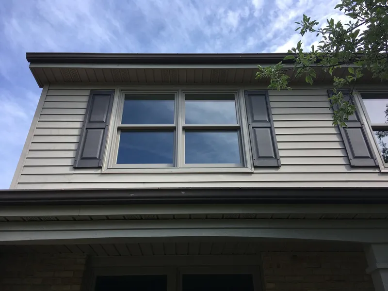 Double window with dark shutters on beige siding.