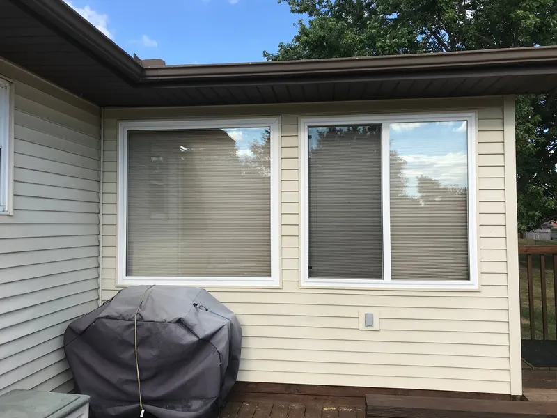 Two white-framed windows in cream siding above a deck.
